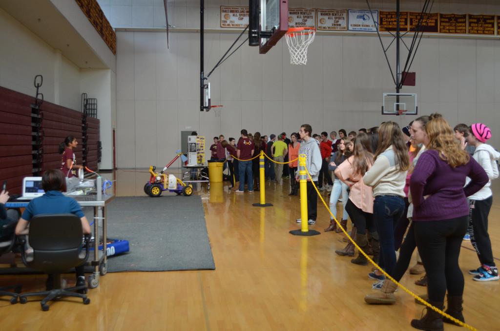 Members of the Robotics Team demonstrate the functions of one of their robots to a crowd of student onlookers.