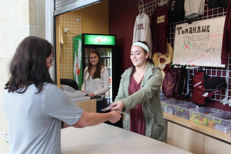 Vice President of DECA Fundraising senior Lexi Brilliant hands a student a candy bar while working a shift at the school store. New Tomahawk apparel and snacks are available for purchase everyday after school.