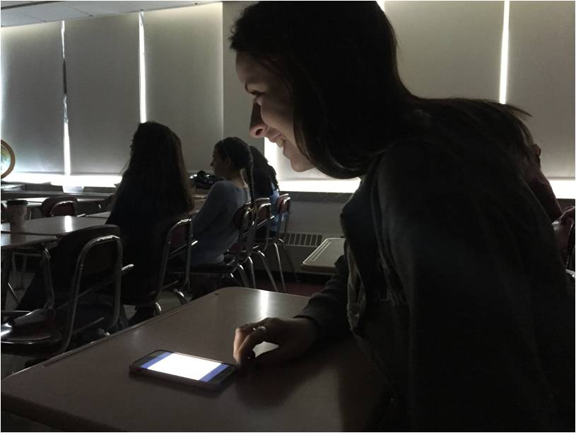 While opening an app on her phone, junior Lizzy Quill laughs at a classmates joke about her not paying attention.