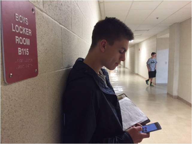 Checking his phone, senior Andrew Travins waits to check in new people before the start of practice.