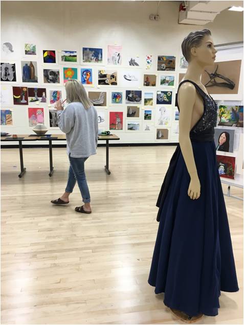 In the background, senior Mackenzie Hostage sips a smoothie while glancing at the hanging art pieces. In the foreground, a mannequin wears junior Max Donahue’s original prom dress design.
