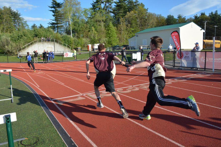 Athletes pass of the baton in the four by 400 relay and sprint toward the finish line. 