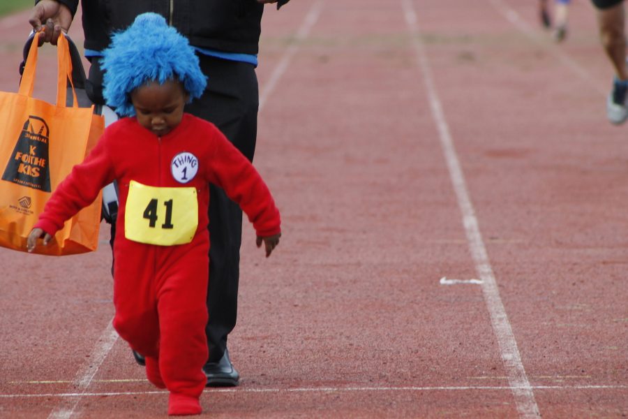 A child from the community dressed up as Dr. Seusss Thing One skips across the track.