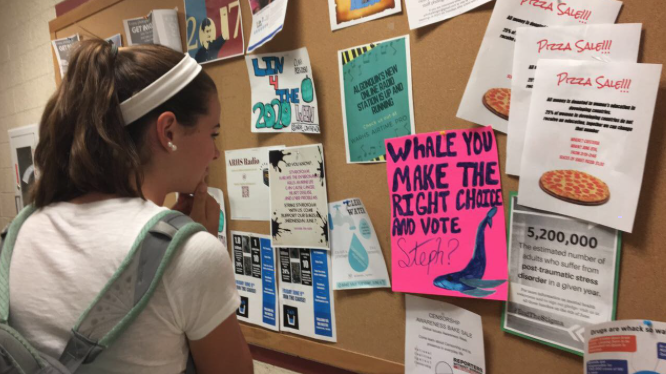 Freshman Ella Kea, scopes out different flyers and campaign posters in the H200 hallway outside the H217 lab.