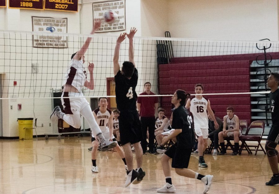 Senior Cam Poutre spikes the volleyball while his opponent jumps up for a block.