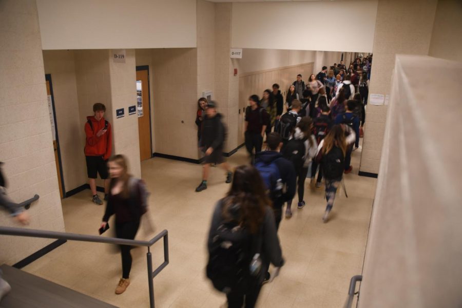 Students walk through the halls during the passing time between classes while junior Jack Poole waits outside of a classroom on his phone.