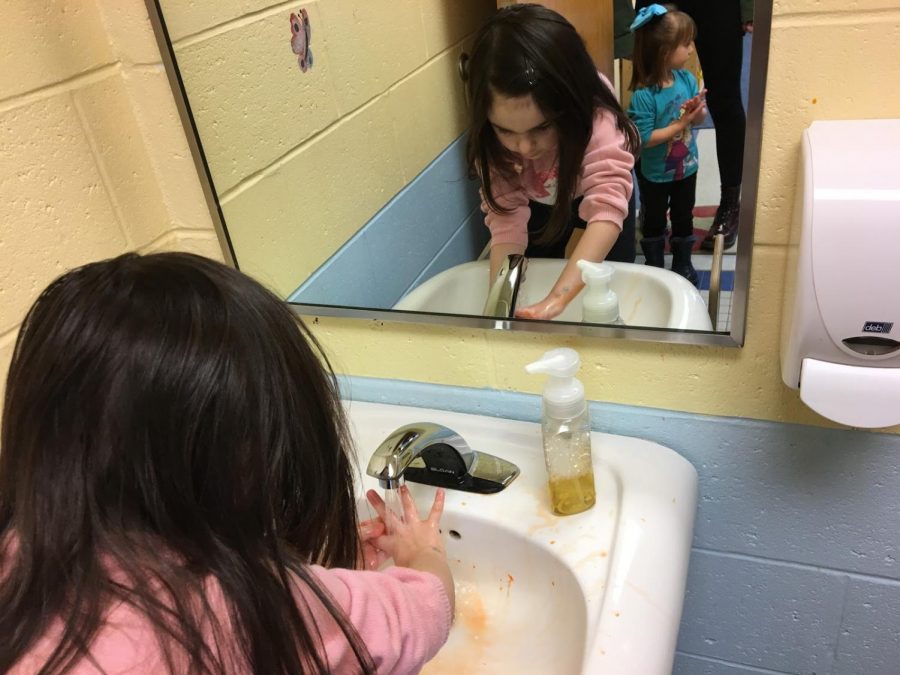 Students wait in line to wash their hands after the penguin project. Lily practices proper hygiene habits by washing her hands after finger painting.