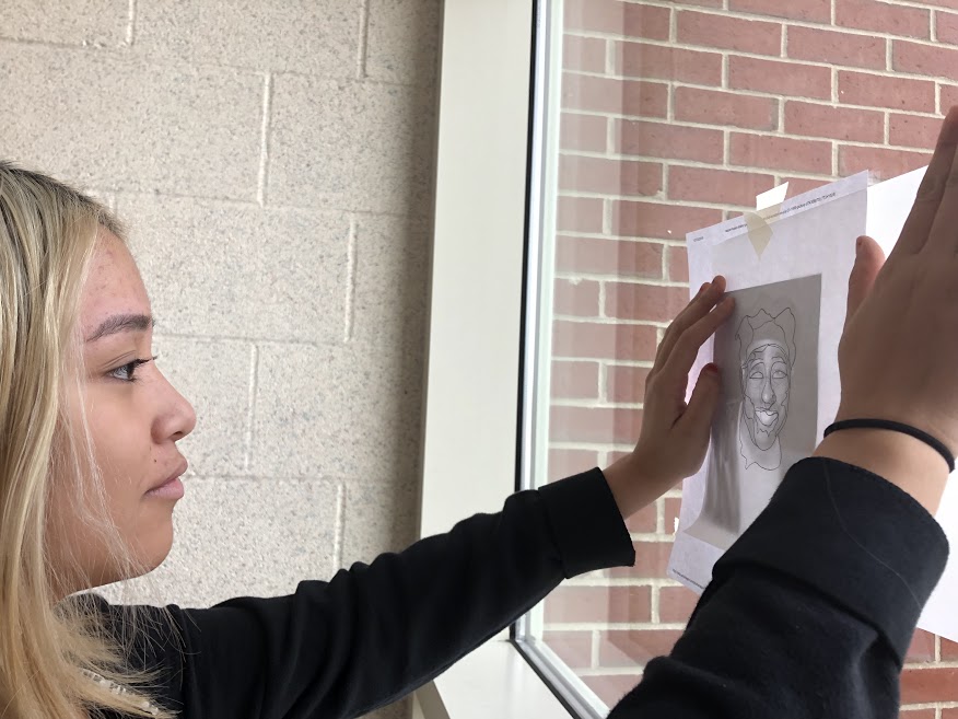 For an art class assignment, freshman Lilia Trevino hangs up her portrait on the window so it is easier to trace the original image.