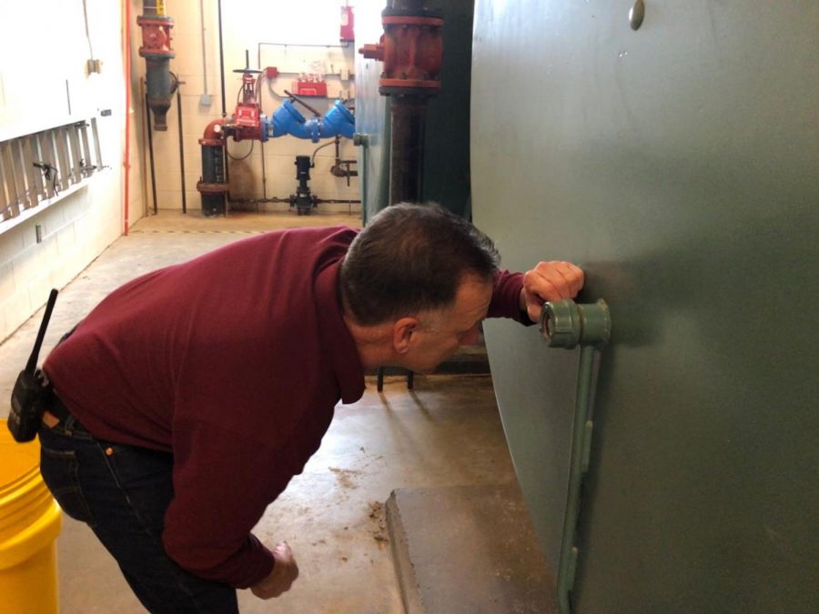 Facilities Director Mike Gorman peeks through the inspection port to see the inside of one of the two boilers In the winter, it costs $2,000 a day to heat the school.