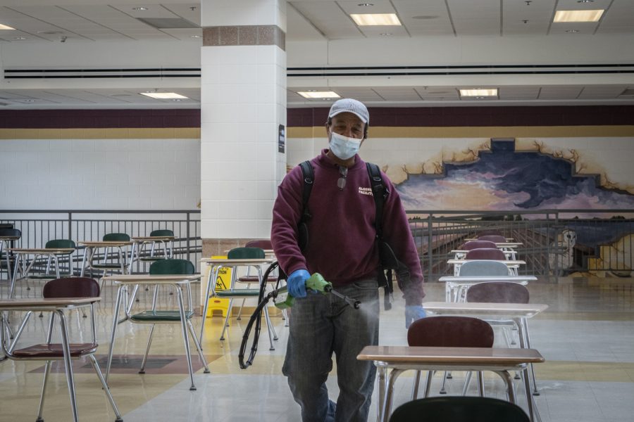 Custodian Jon Souza flashes a quick smile through his mask while sanatizing the cafeteria. The sanitization of cafeteria surfaces is one of the cleaning protocols the school has recently invested in.