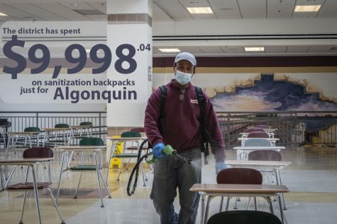 Custodian Jon Souza uses a new electrostatic sprayer to sanitize cafeteria desks. Sanitization of cafeteria surfaces is one of the new cleaning-related expenses this year.