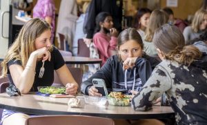 Students eat lunch while conversing with their peers. 