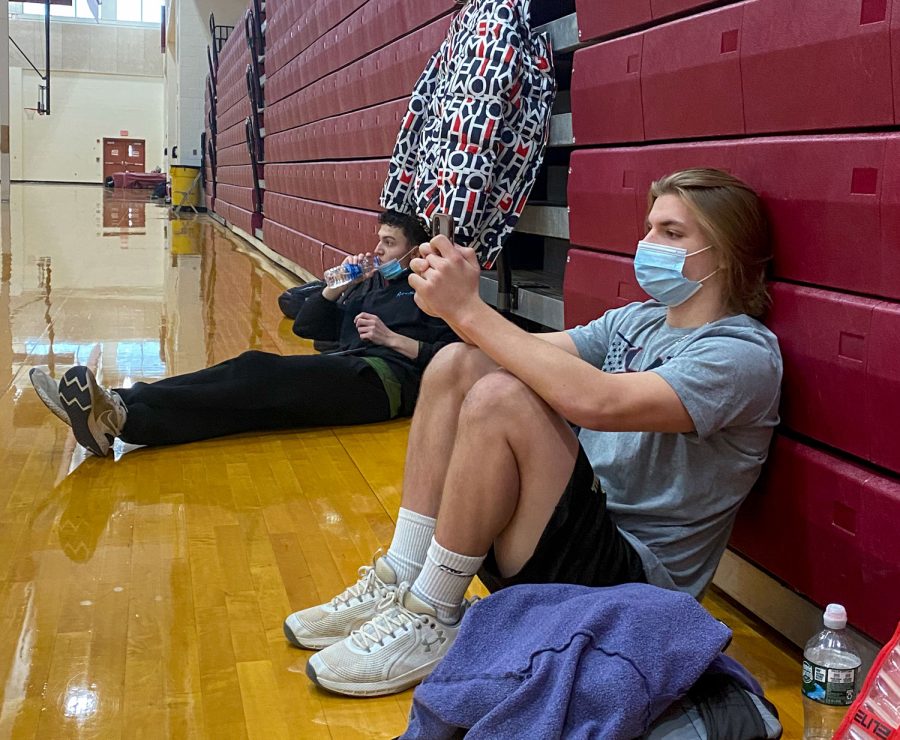 Senior Jason Levin (right) checks his phone, fully-masked, while waiting to be subbed into the soccer match. Senior Adam Mowry (left) lowers his mask to drink water after subbing out of the game.