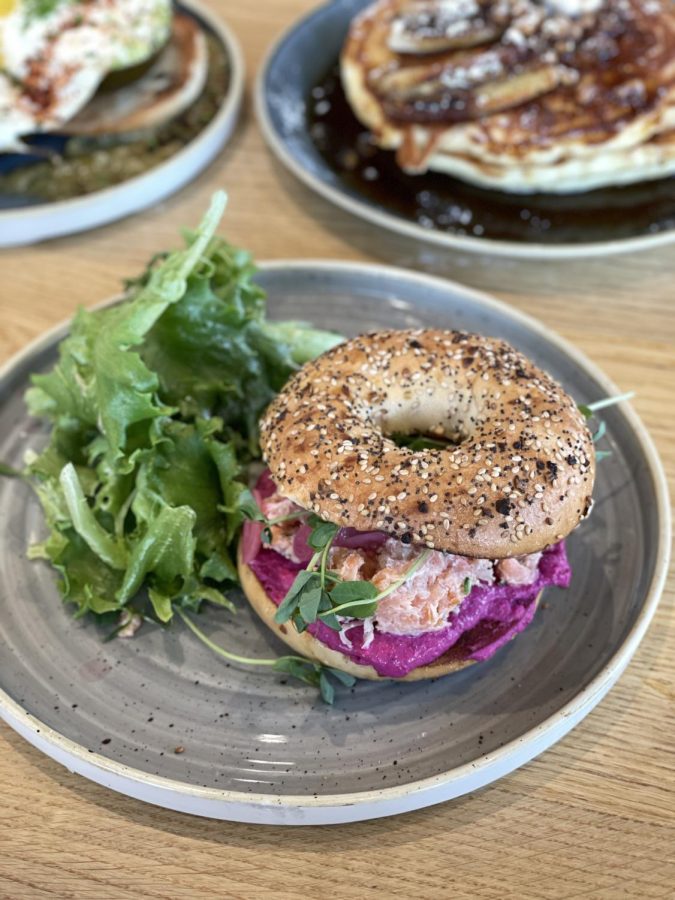 The Smoked Salmon Smear + Bagel dish is filled with beet cream cheese smoked salmon with a side of leafy greens. 
