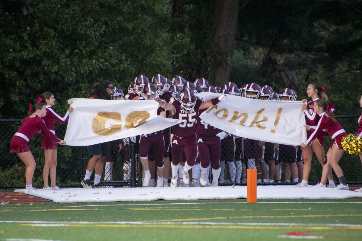 Senior captain Dom Frallicciardi (55) runs through a banner held up by the cheerleaders that reads "Go Gonk" during their 31-14 loss against Doherty  on Sept 13.