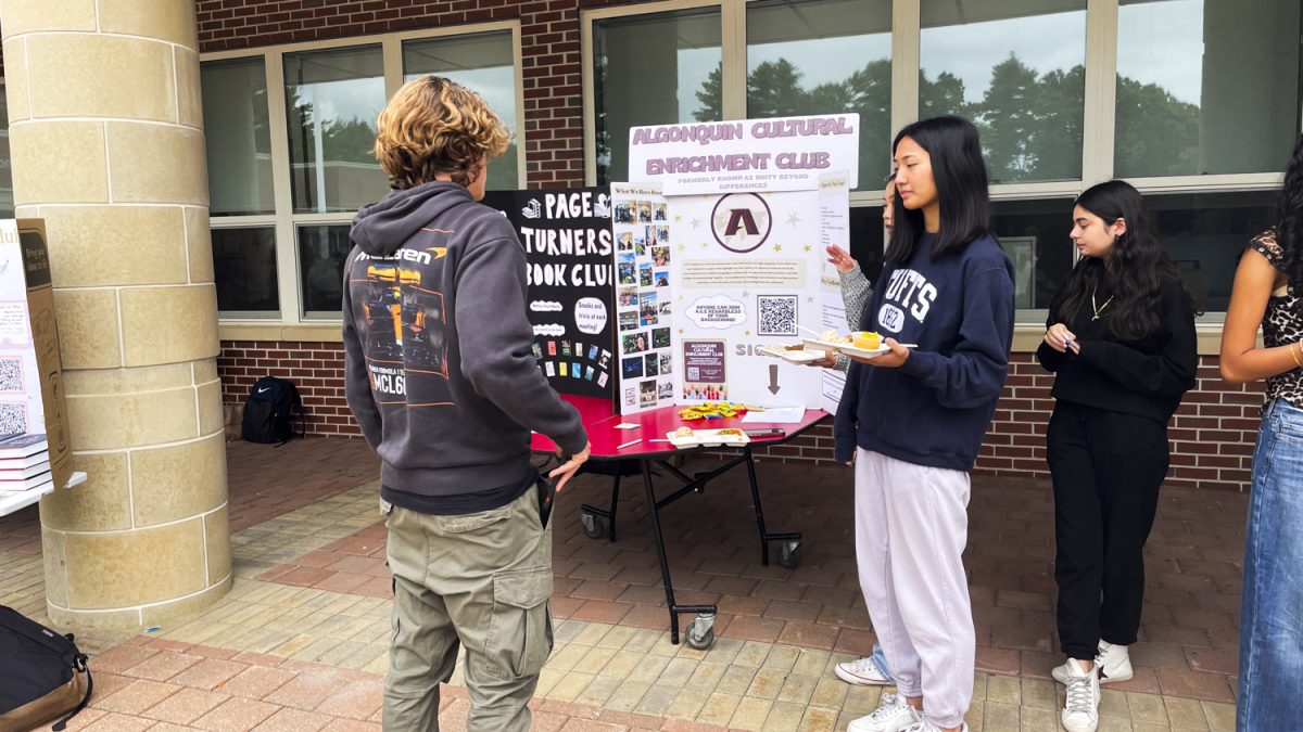 Freshman Mika Harmson (left) pulls out his phone to scan a QR Code after reading the Cultural Engagement Club poster and listening to junior Sophia Shen (right) talk about the activities available.