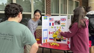 Sophomore Amy Li (middle) explains the Model UN Club to freshman Ryan Kemp (left) while junior Hannah Nealon (right) pours Sour Patch Kids to attract students to the stand at the Club Extravaganza on Sept. 23, 2024.