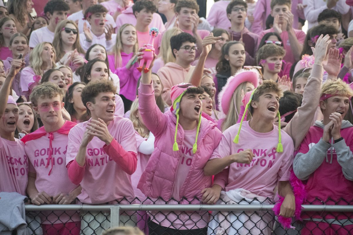 On Oct. 11, senior Zach Ruthfield (center holding a pink chicken) cheers for the Algonquin football team with other students dressed for the theme, Pink-Out, during their win against Shepherd Hill.