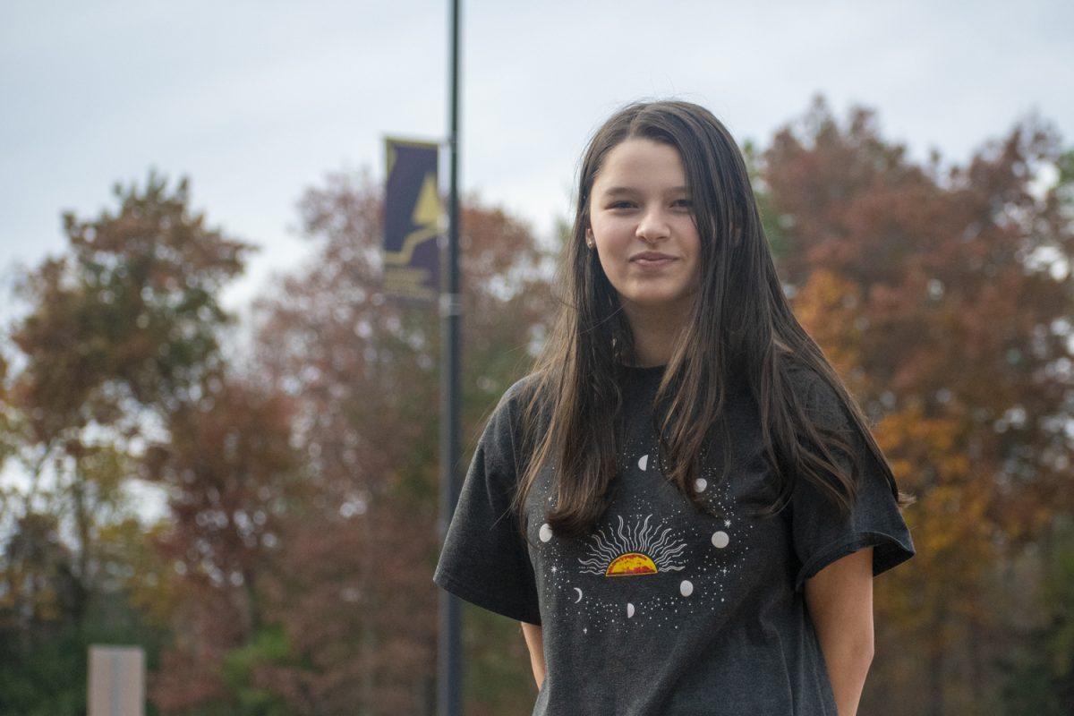 Senior Lillian Johnson stands infront of a banner she designed, incorporating the new Algonquin logo into her design.