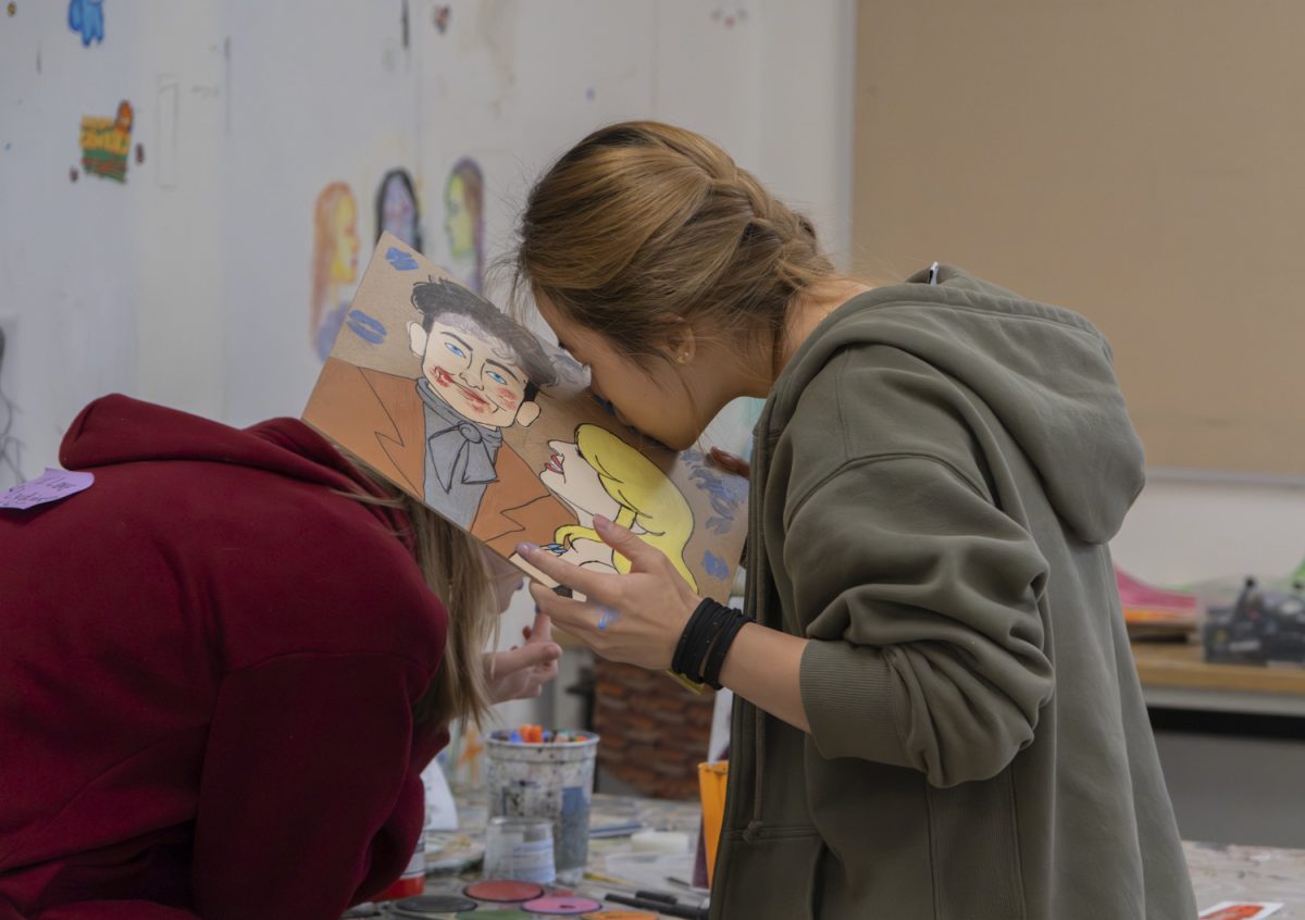 Senior Adrienne Li helps fill in the background of her friend's art project by kissing it with blue face paint on her lips.