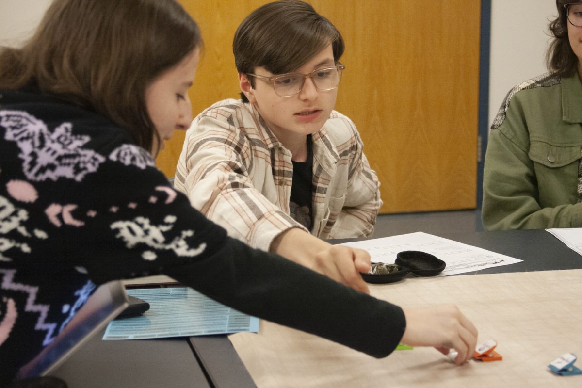 Club leader and game master junior Mia Murphy moves the game pieces in order to create the diversions of sophomore Linq Kaelin's move during a DND club meeting.