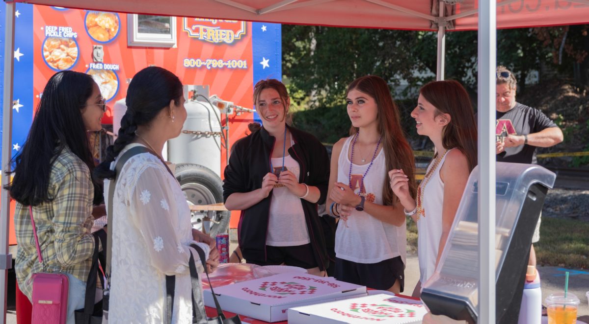 During the 35th annual Applefest on Sept. 20, members of the Algonquin Cheer team: seniors Chloe Jewers, Clarissa Truman and sophomore Isabella Gallini sell pizza to senior Kartiki Sarangdhar at the street fair.