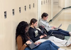 Sophomores Nathalia Souza and Samantha Randall and freshman Cara Saks, students in Spanish Teacher Pauliny Smith’s Spanish II class, work on their end-of-unit project in the hallway on March 11. Students in Smith’s classes and other foreign language classes often use the hallway and locker spaces to work on assignments.
